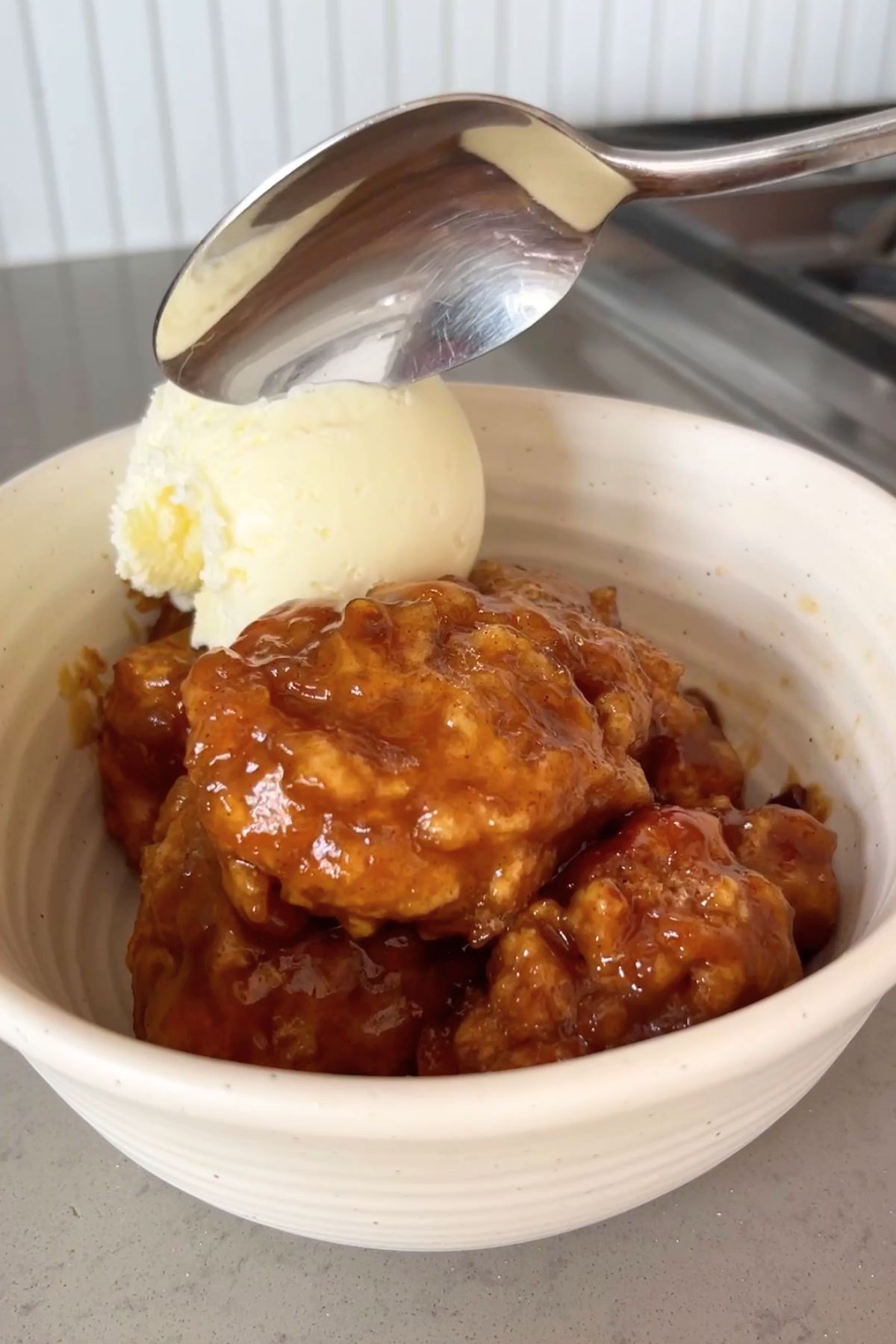 Sticky golden dumplings served in a bowl with a scoop of vanilla ice cream and a spoon ready to dig in.