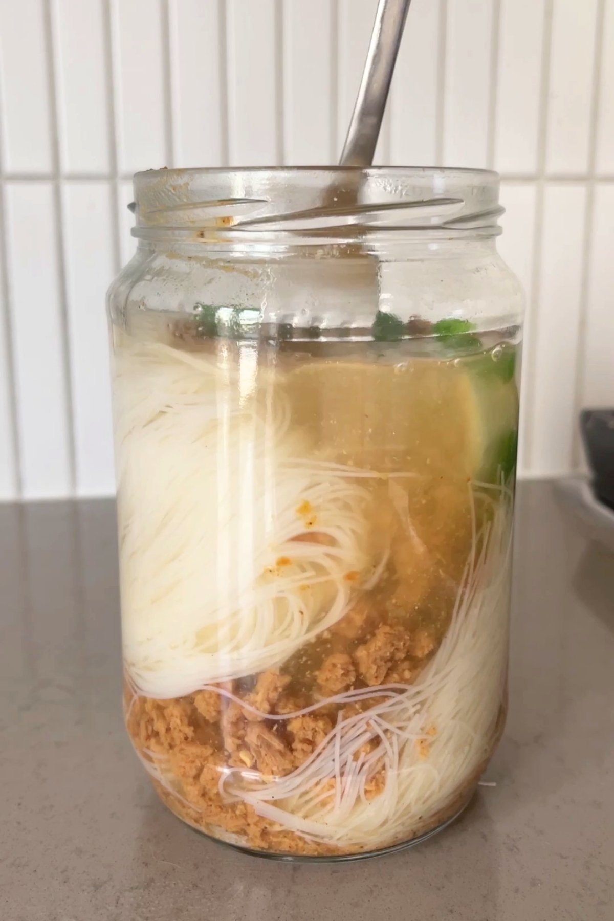 Boiling water poured into a jar of dry noodles, TVP, and vegetables, starting to soften the ingredients and create broth.