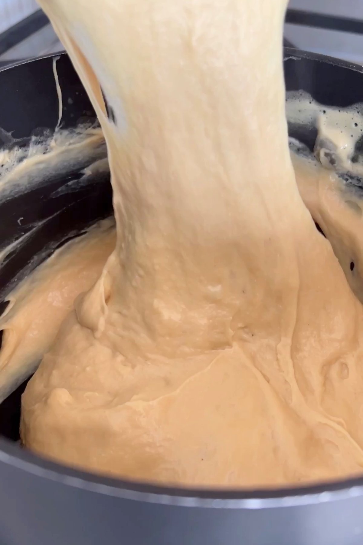 Thick, stretchy vegan cheese mixture being lifted from a saucepan in a smooth, melty ribbon.
