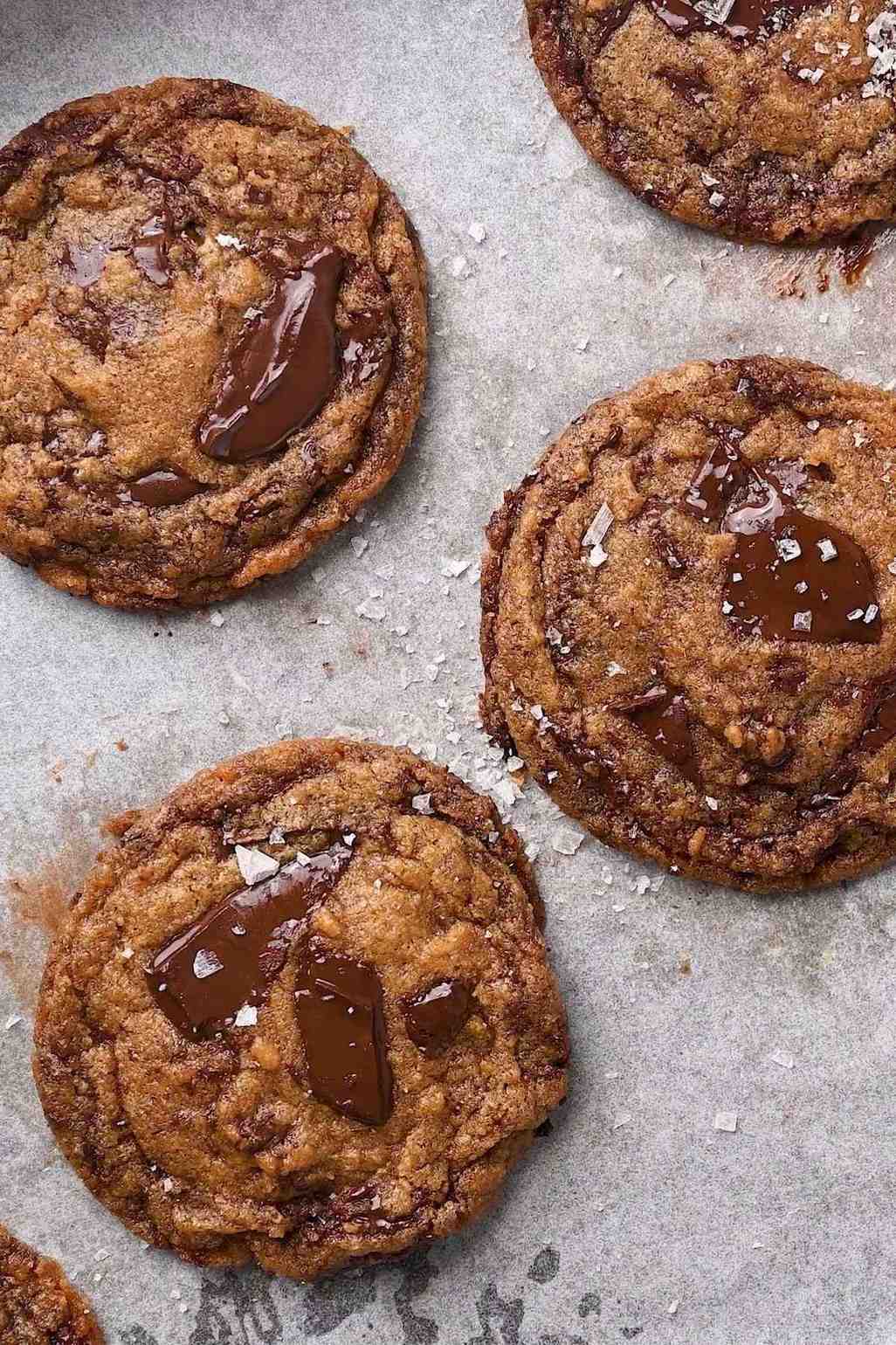 Warm chocolate chip cookies resting on parchment, with melted chocolate pools and a sprinkle of salt flakes.