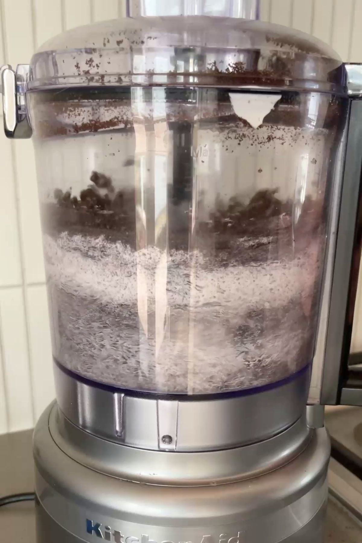 Crushed Oreos and cream cheese being blended in a clear food processor bowl on a silver base.