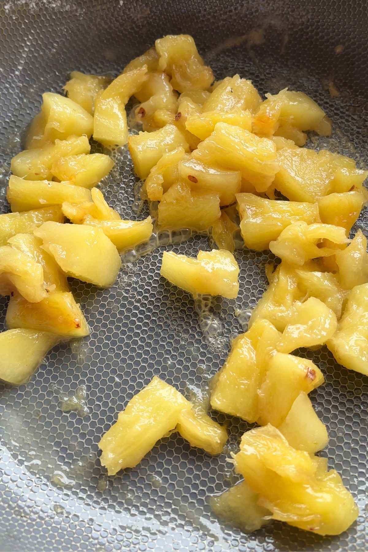 Glossy pineapple chunks cooking down in a pan, juices bubbling lightly.