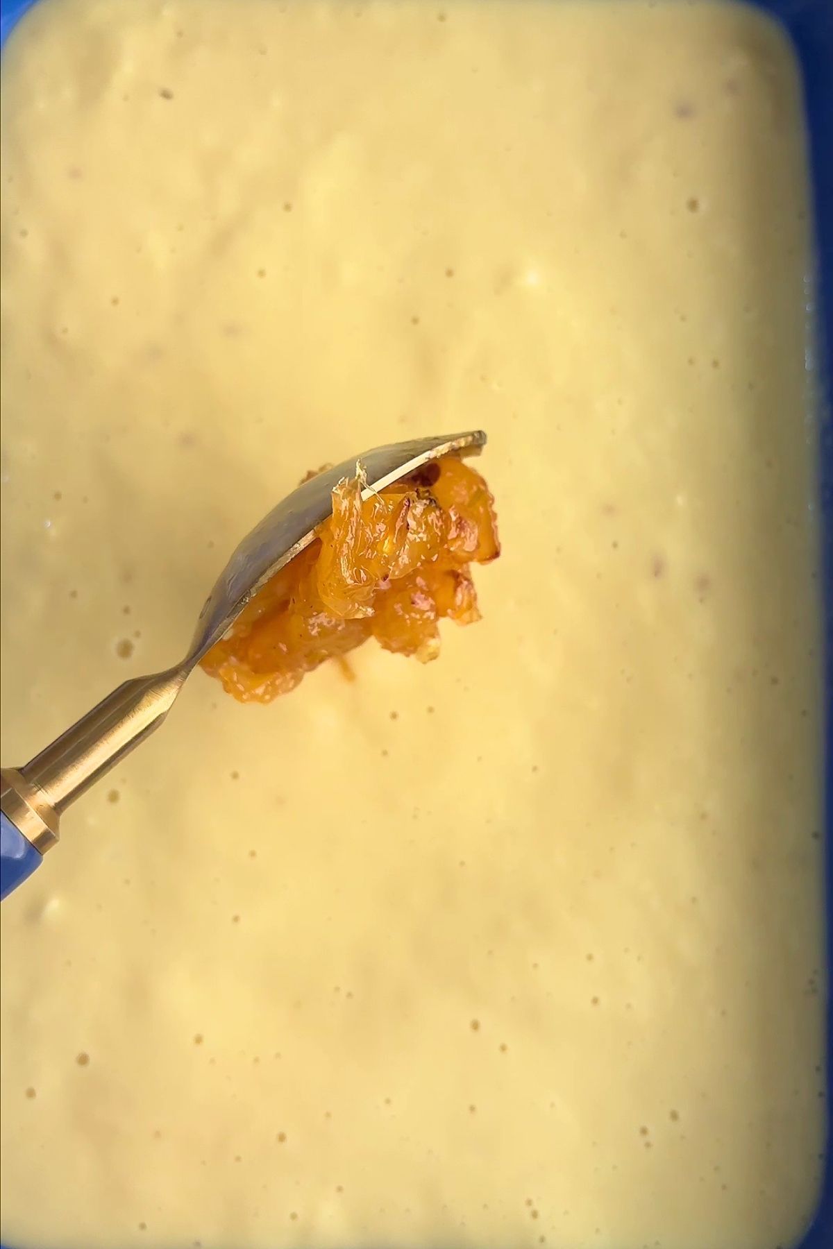 Caramelized pineapple swirl being spooned over blended ice cream base in a container.