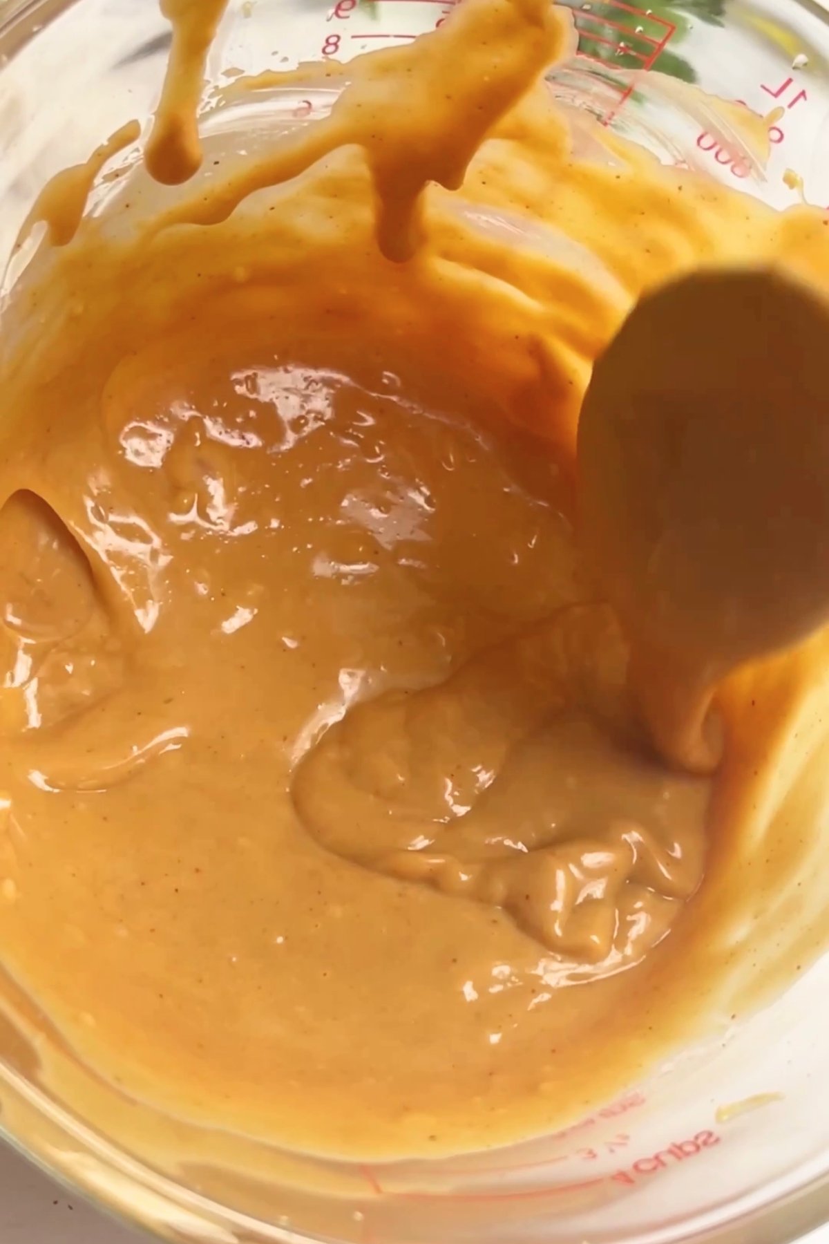Thick golden peanut sauce being stirred in a glass measuring jug.
