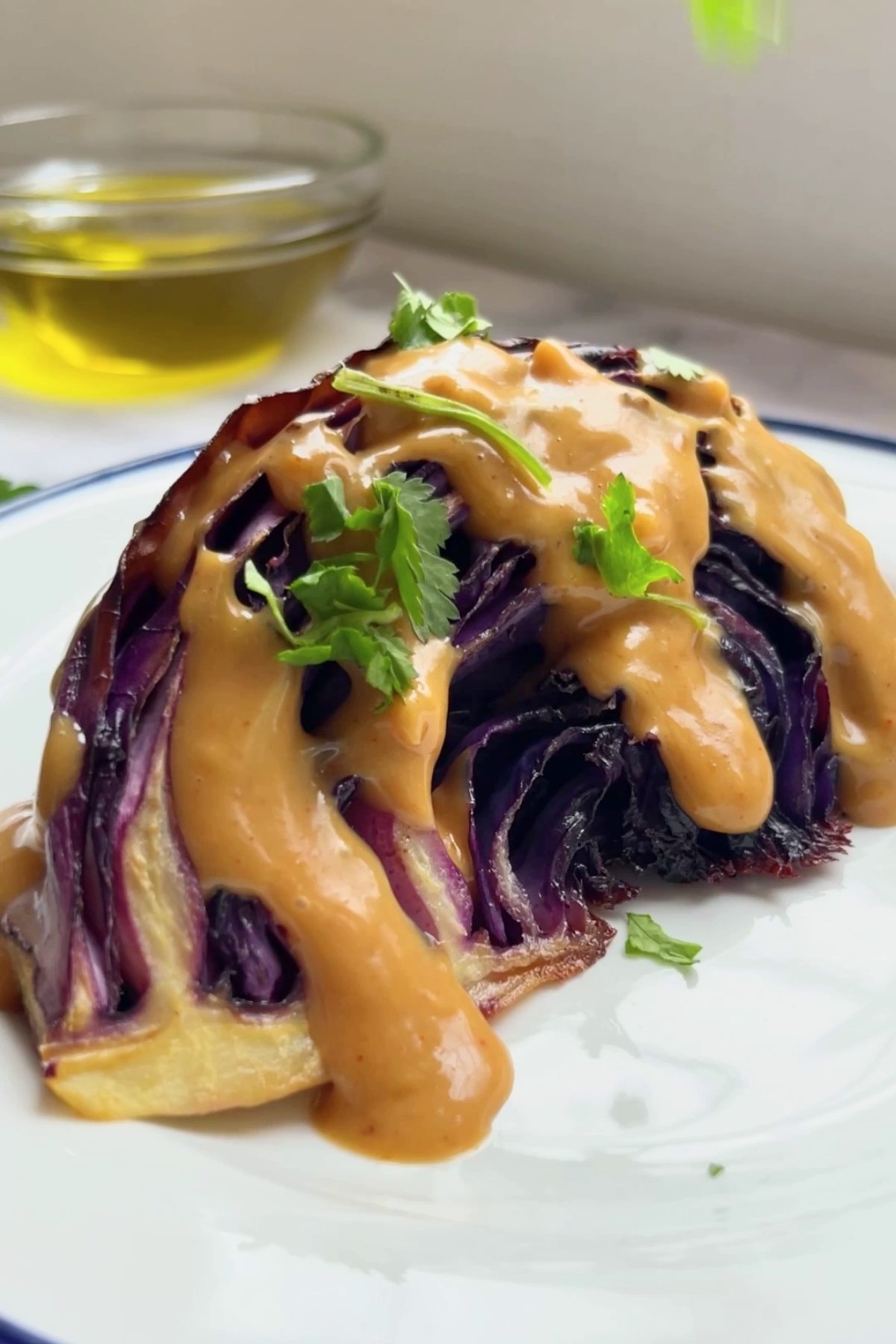 Roasted red cabbage wedge topped with thick peanut sauce and fresh coriander leaves on a white plate.