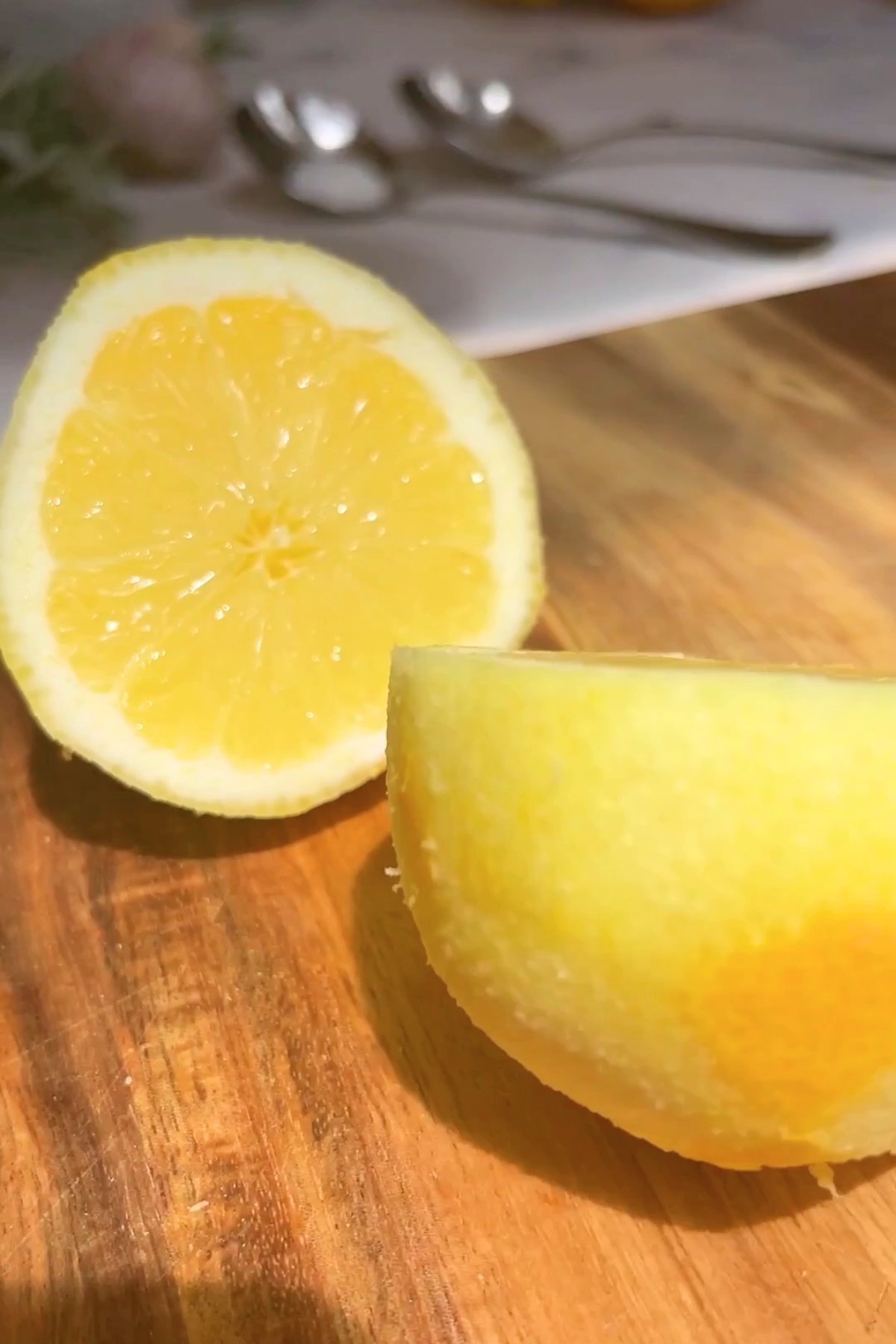 Two lemon halves resting on a wooden board, one showing the juicy interior and the other with textured yellow peel.
