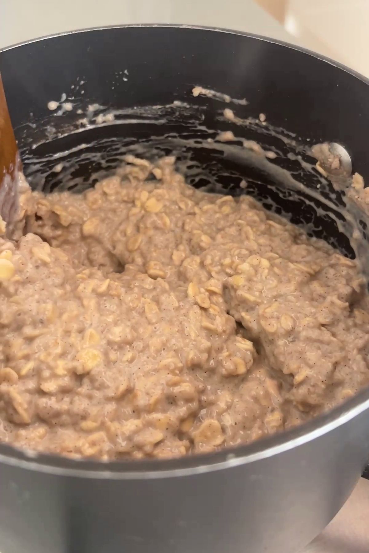 Thick, creamy oat and chia porridge being stirred in a saucepan, with visible flecks of spice throughout.