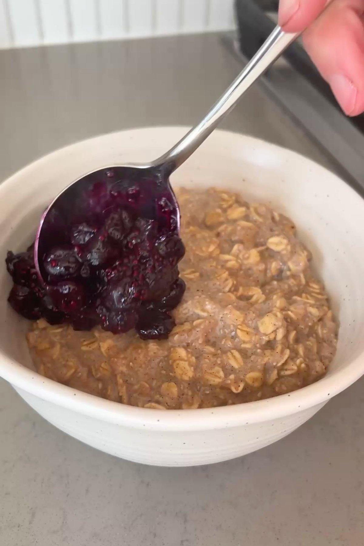 Spoonful of glossy blueberry chia compote being added to a bowl of spiced oat porridge.