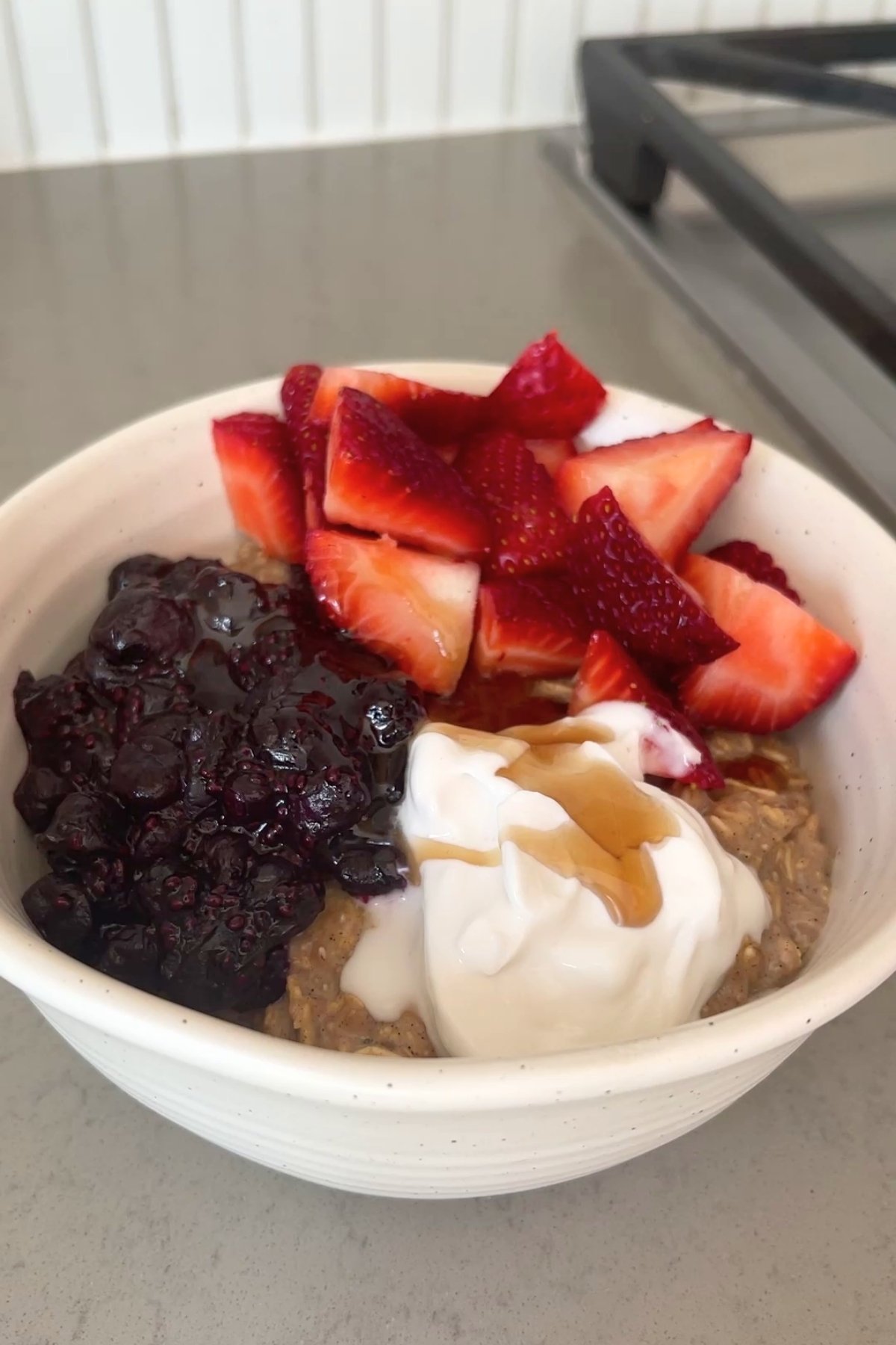 Finished bowl of chia oat porridge topped with blueberry compote, fresh strawberries, coconut yogurt, and a drizzle of maple syrup.