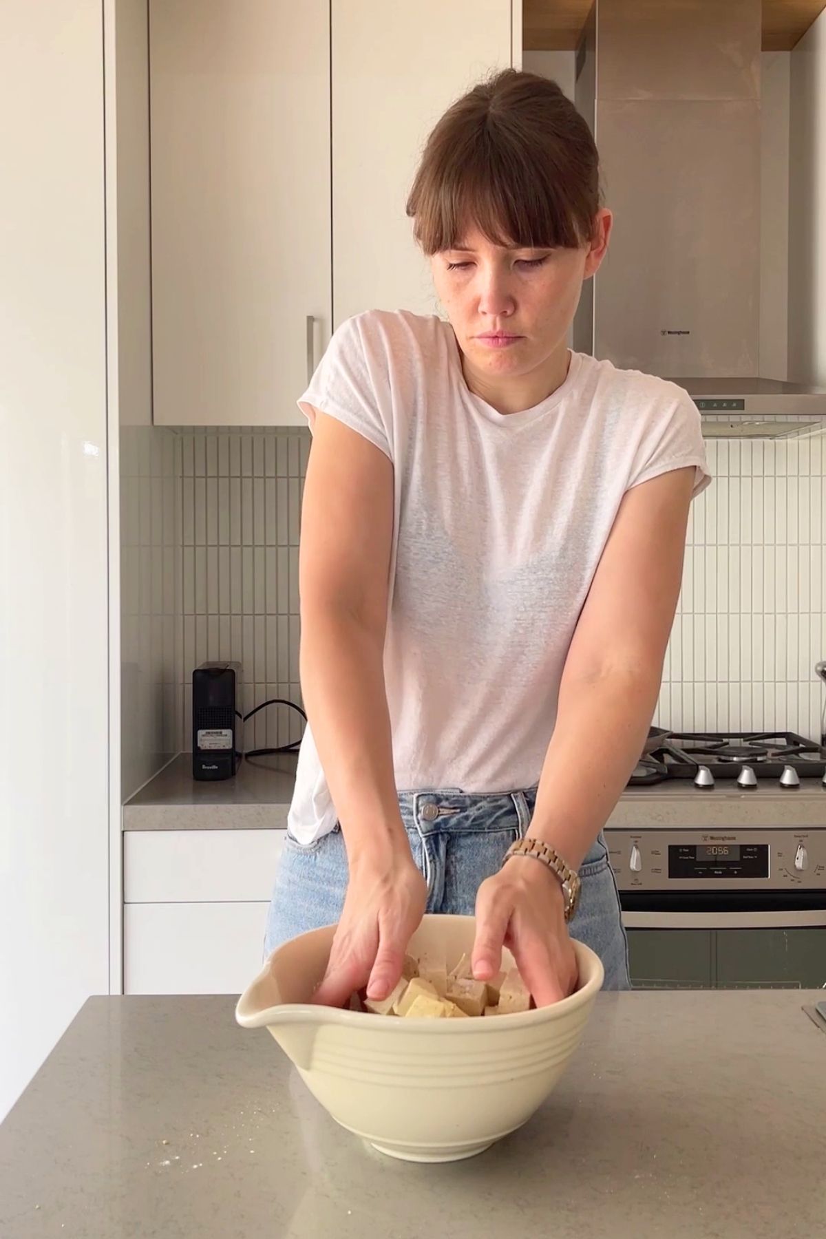 Hands coating cubed tofu in a white mixing bowl.