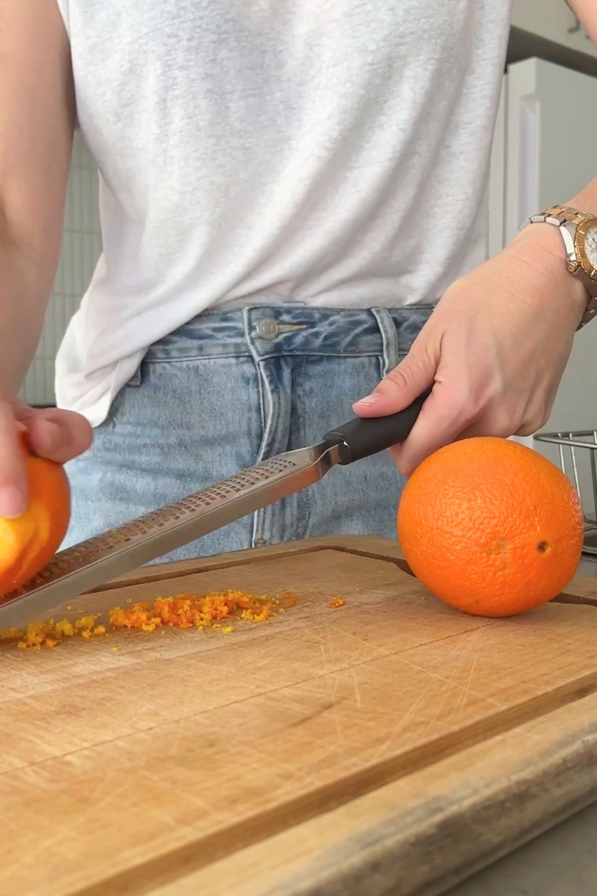 Hands using a fine grater to zest an orange over a wooden board.