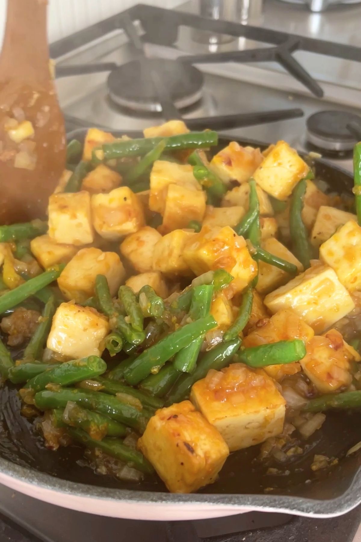 Cubed tofu and green beans coated in glossy sauce in a hot skillet.