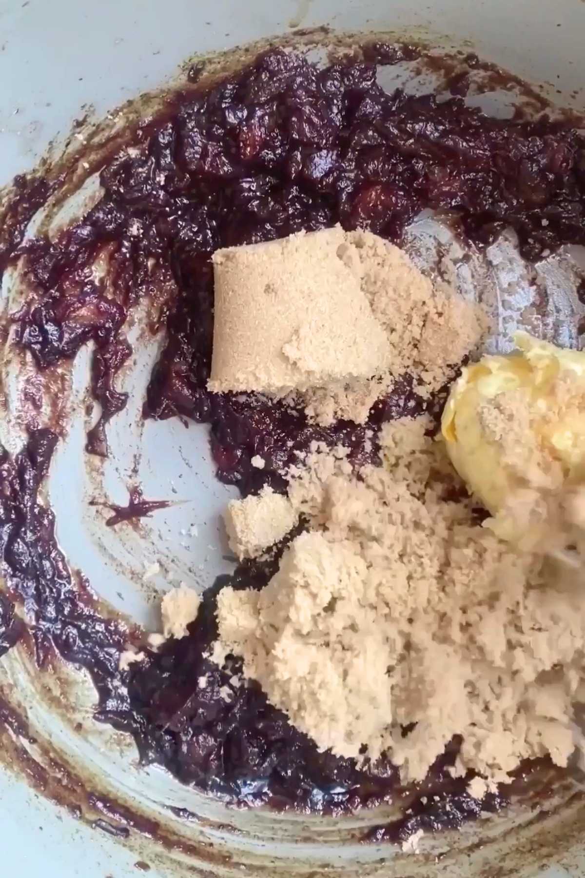 Brown sugar and a pat of butter sitting on a dark date mixture in a pan.