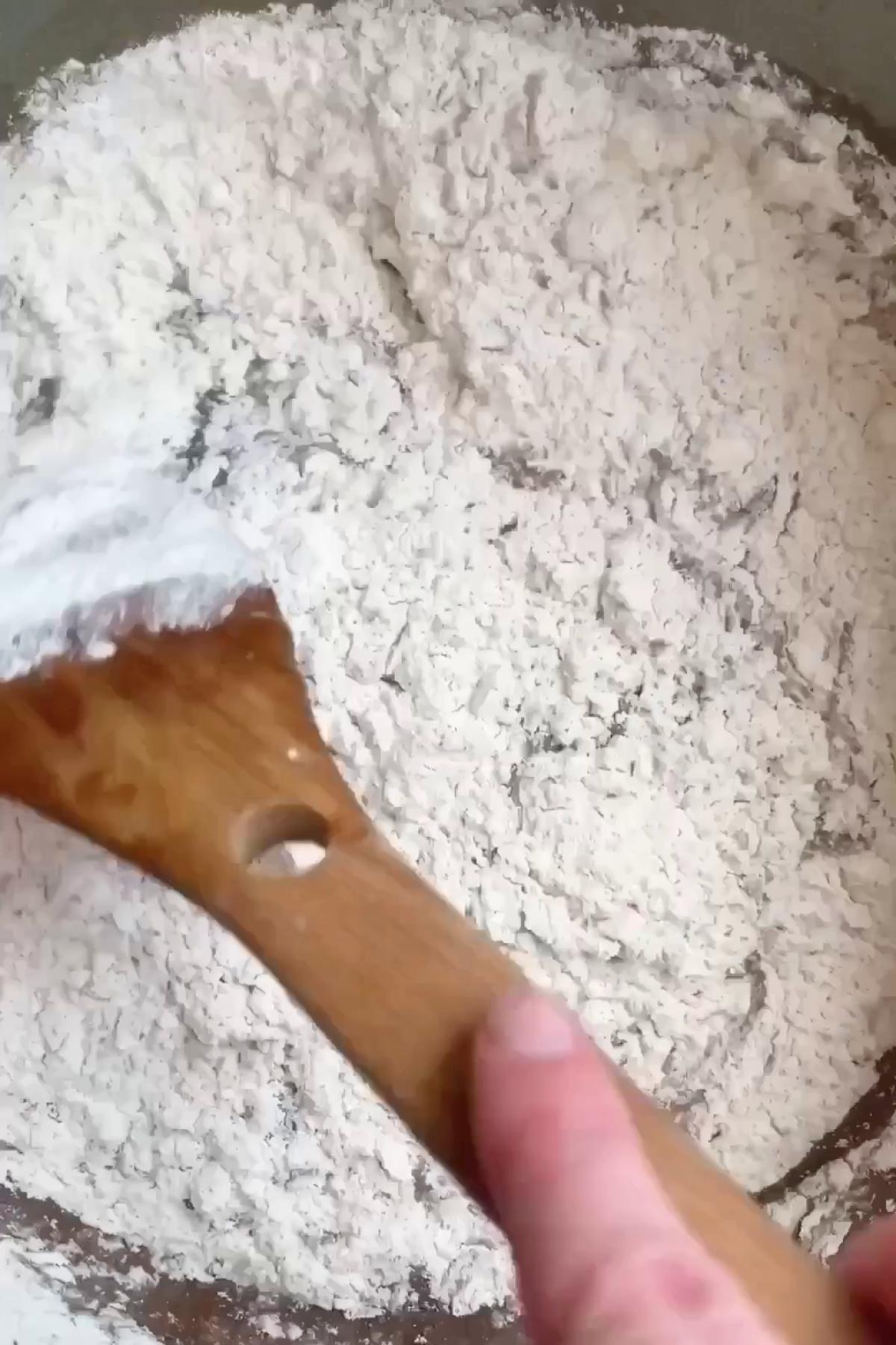 White flour mixture being stirred with a wooden spatula in a mixing bowl.