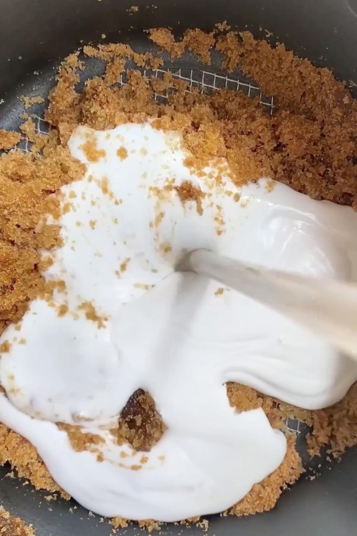 White liquid being stirred into golden sugar granules in a saucepan.