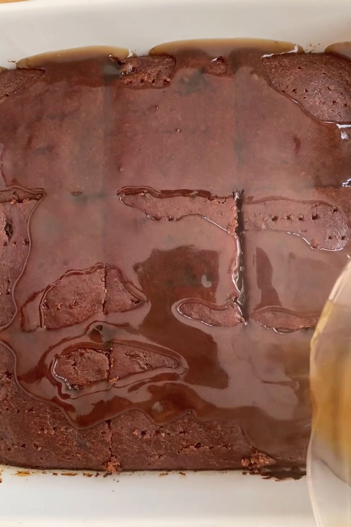 Brown sauce pouring over cut pudding squares in a white baking dish.