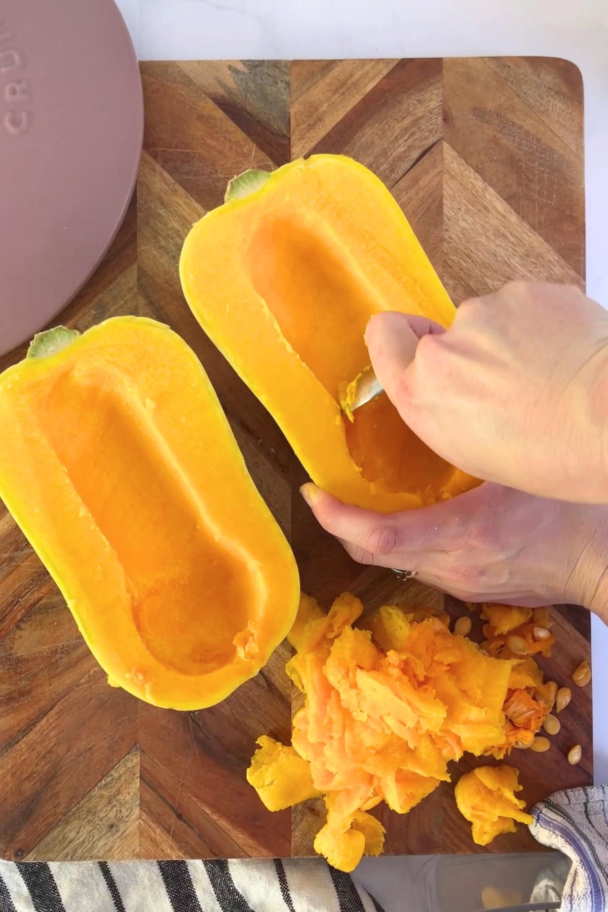 A halved butternut pumpkin being hollowed out with a spoon.