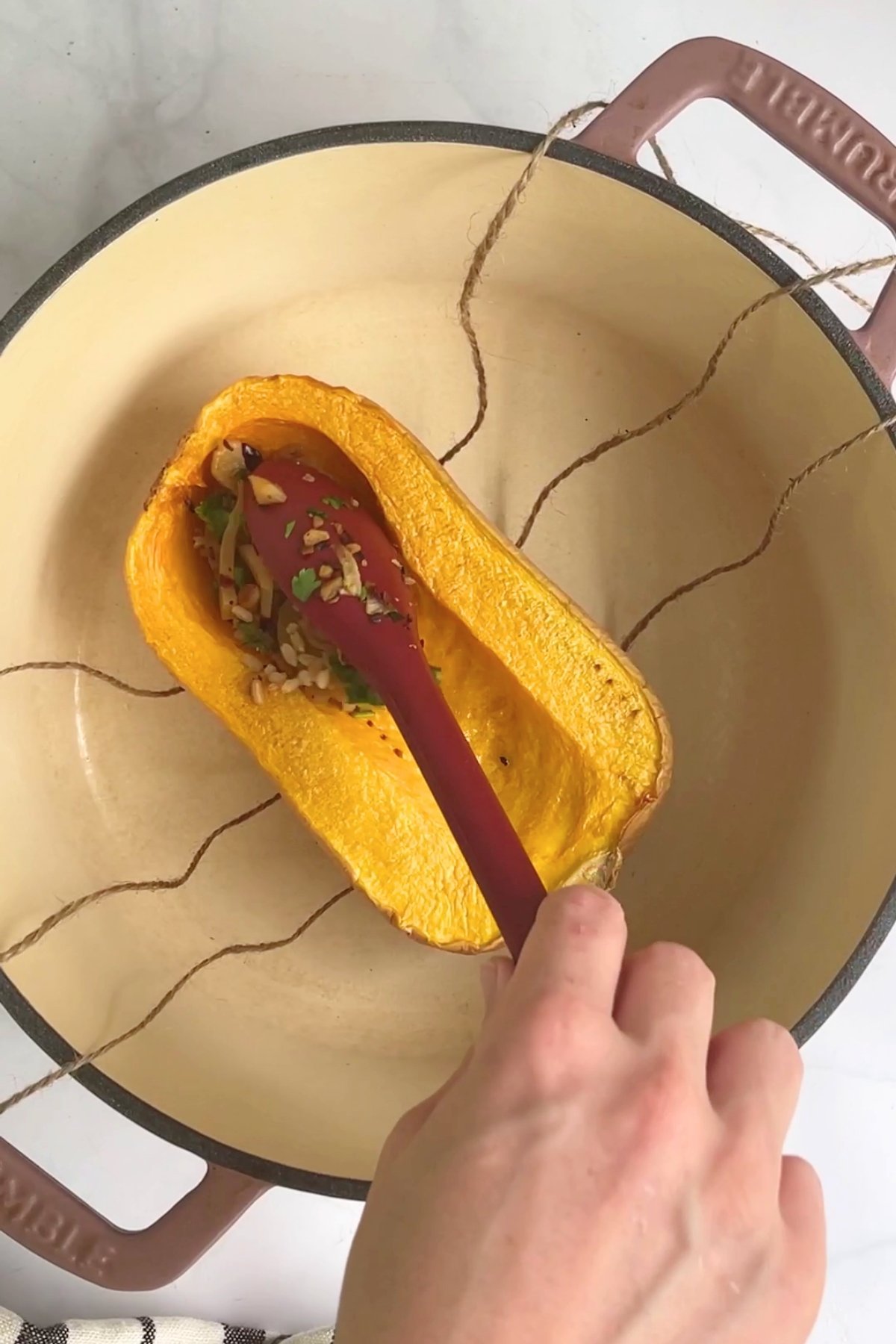 A roasted butternut pumpkin half being filled with stuffing inside a Dutch oven lined with kitchen twine.