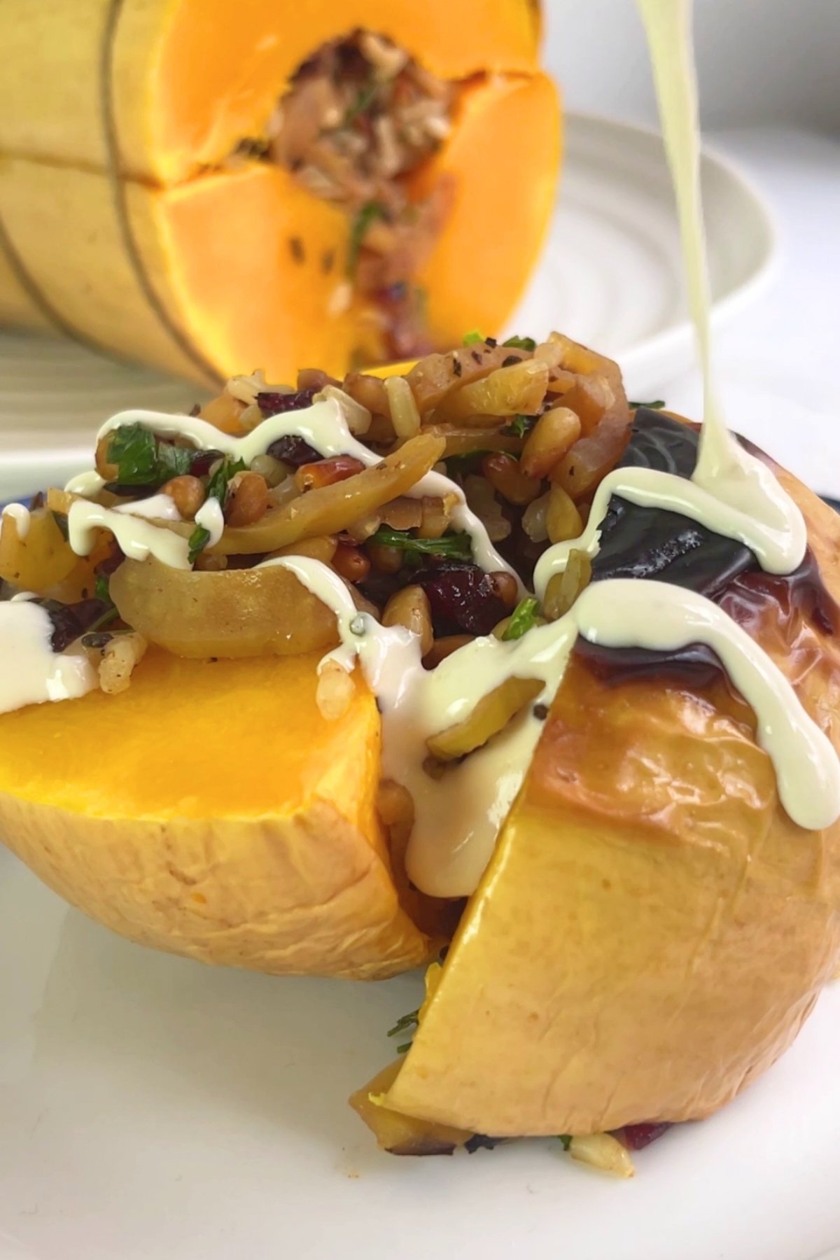 Sliced roasted pumpkin filled with rice and vegetables, drizzled with creamy white sauce on a white plate.