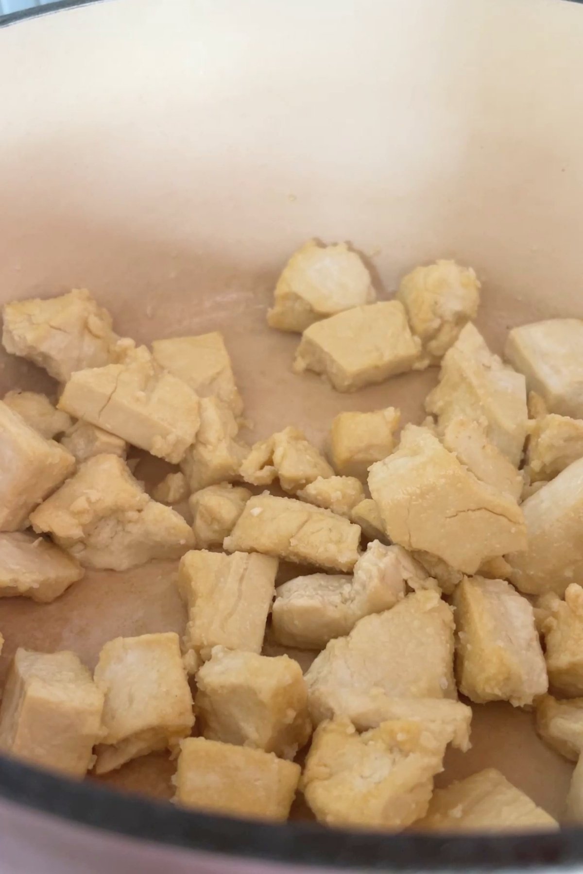 Cubed tofu pieces coated in a light batter frying in the bottom of a beige saucepan.