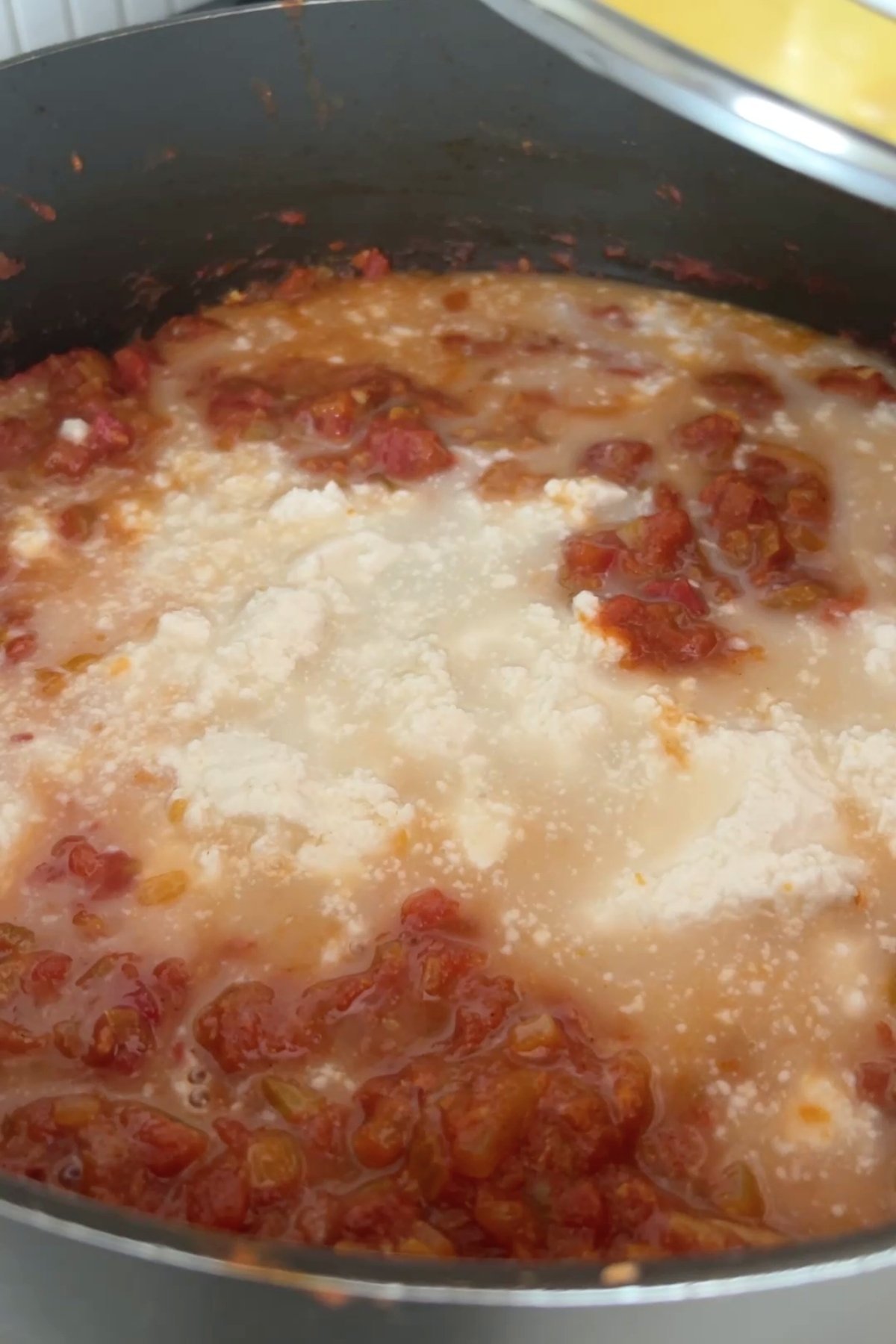 Coconut milk added to a simmering tomato mixture in a black saucepan, creating a creamy, marbled surface.