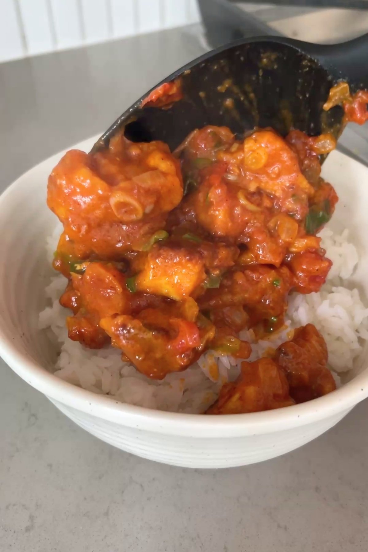 Spoonful of rich, red tofu curry being served over a bowl of fluffy white rice.