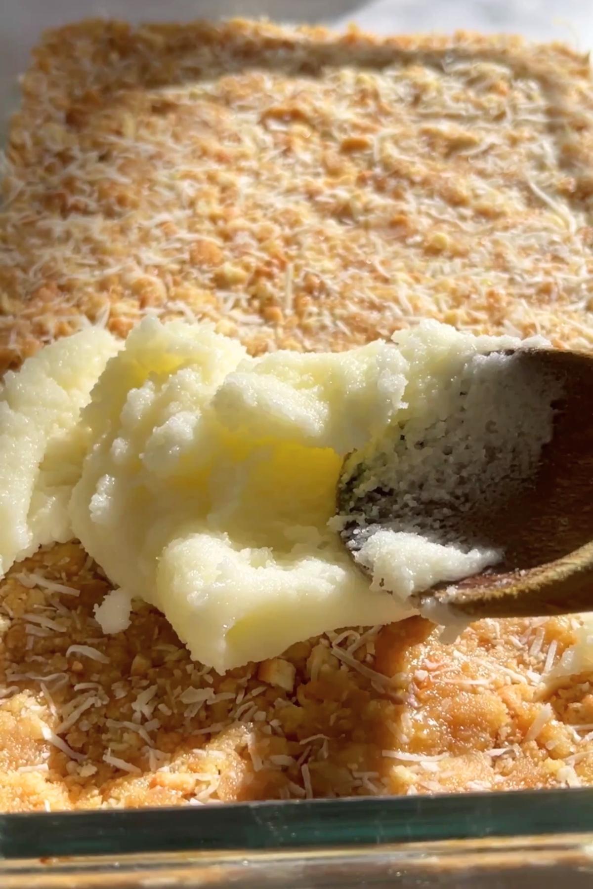 Glaze is being spread over a chilled biscuit and coconut base using a wooden spoon.