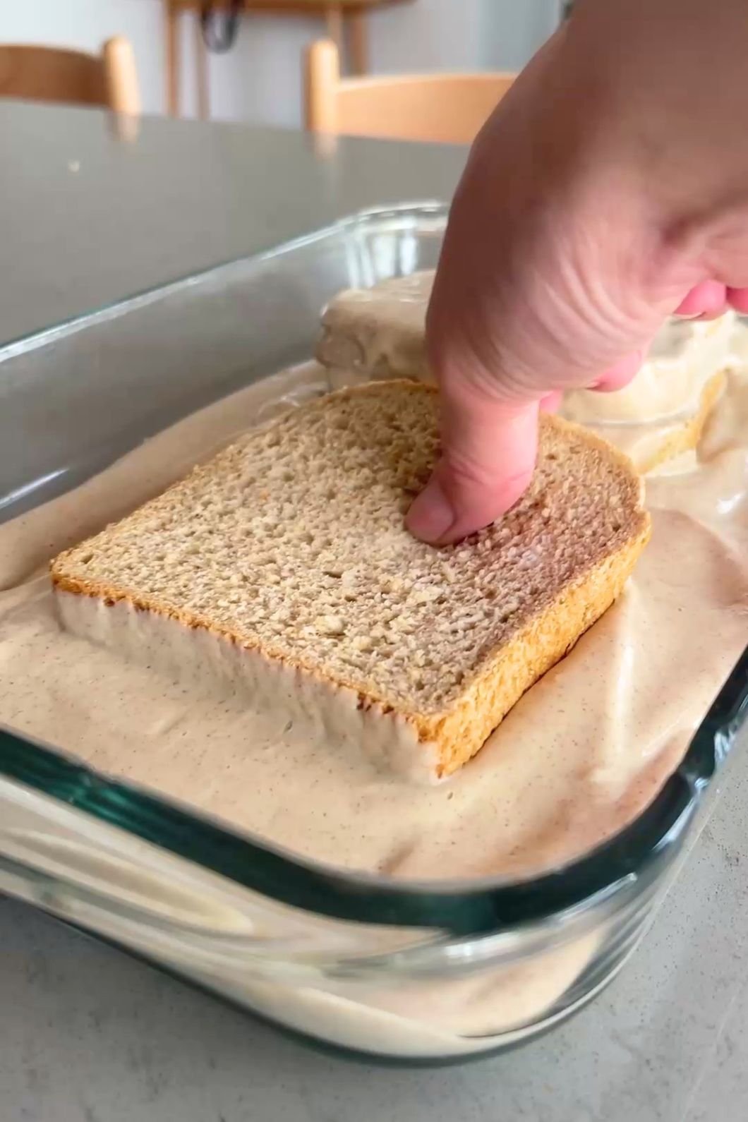 Hand pressing bread into creamy batter dish.