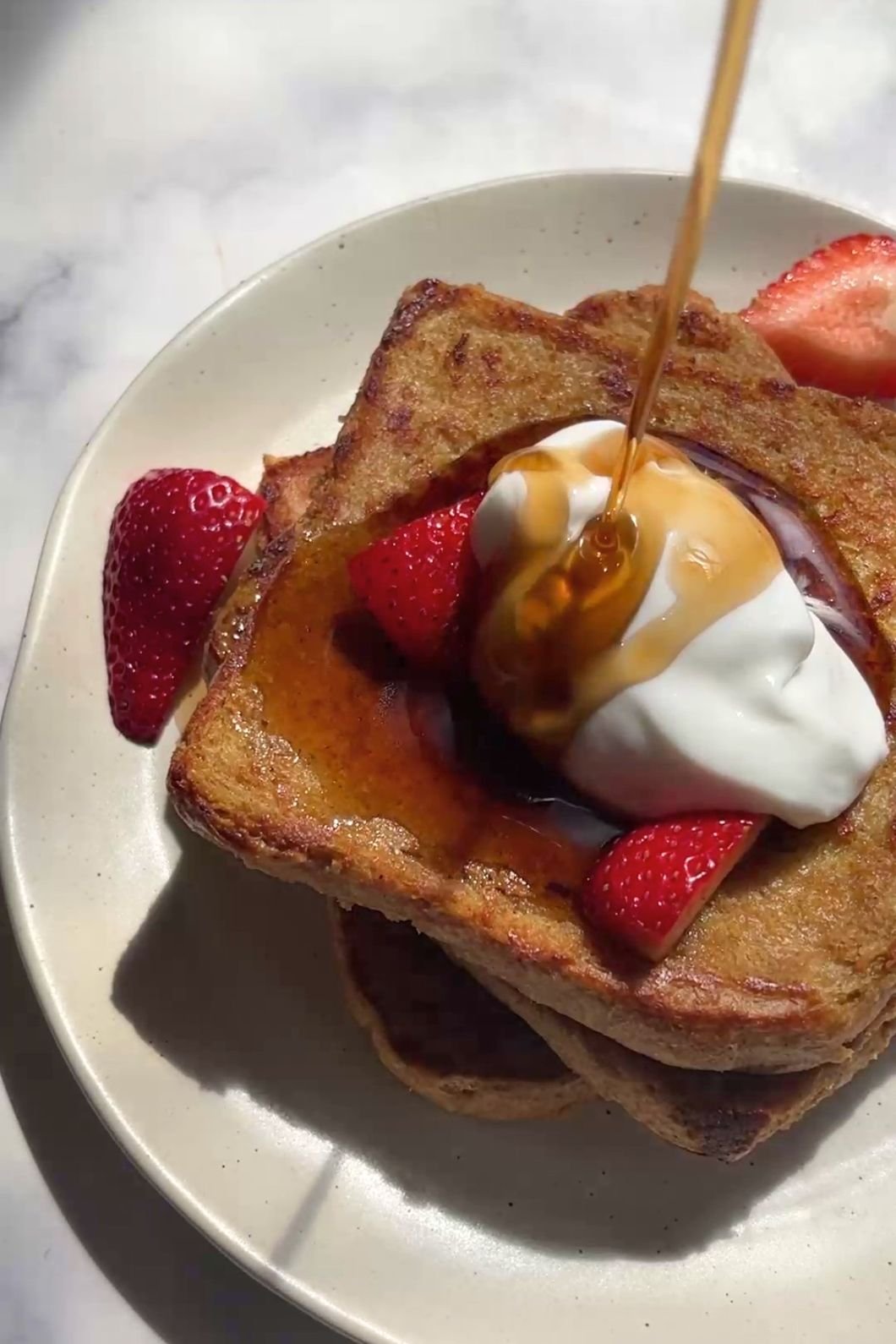 Maple syrup pours over yogurt strawberry toast.