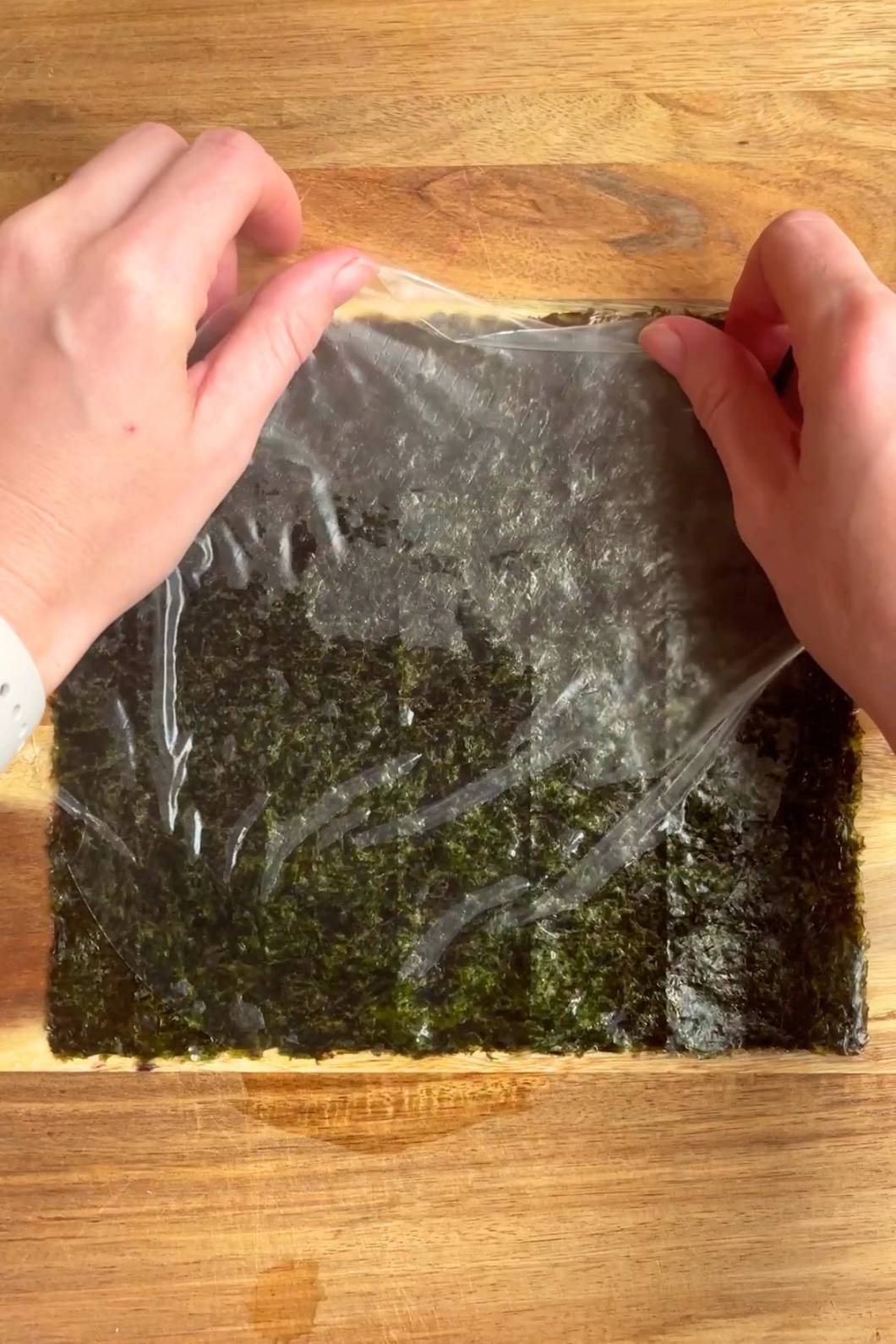 Hands adding softened rice paper on a dark green sheet on a wooden board.