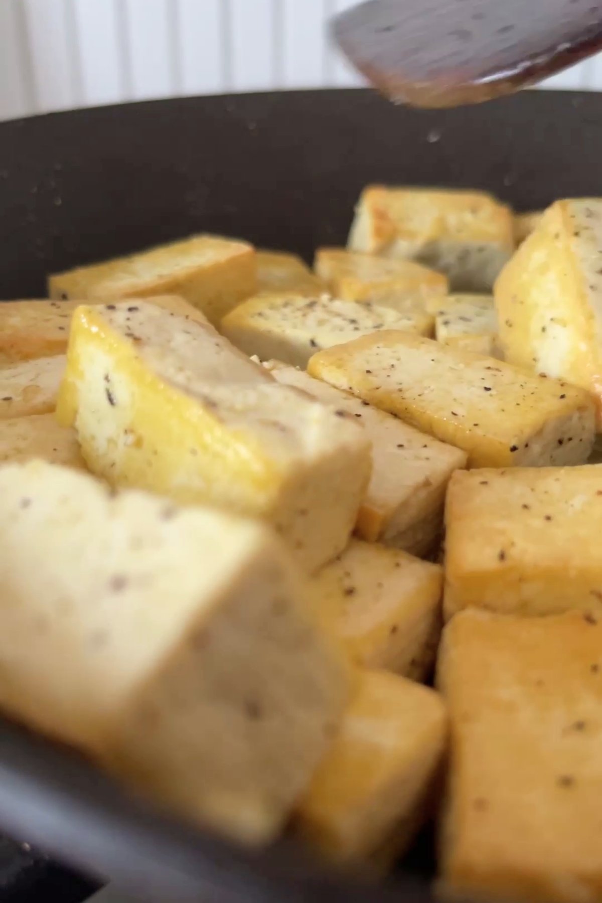 Golden tofu cubes sizzling in a pan, lightly seasoned with cracked black pepper and salt.