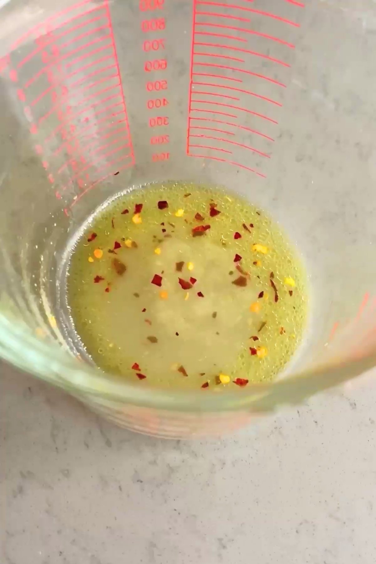 Lime dressing with red chili flakes pooled at the bottom of a glass measuring jug.