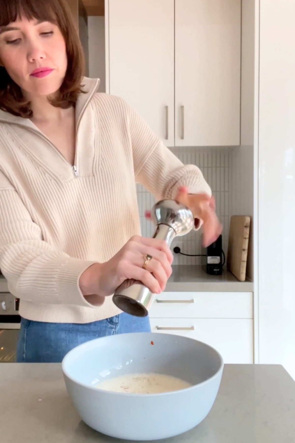 A woman grinding black pepper into a large blue bowl of vegan buttermilk mixture on the counter.