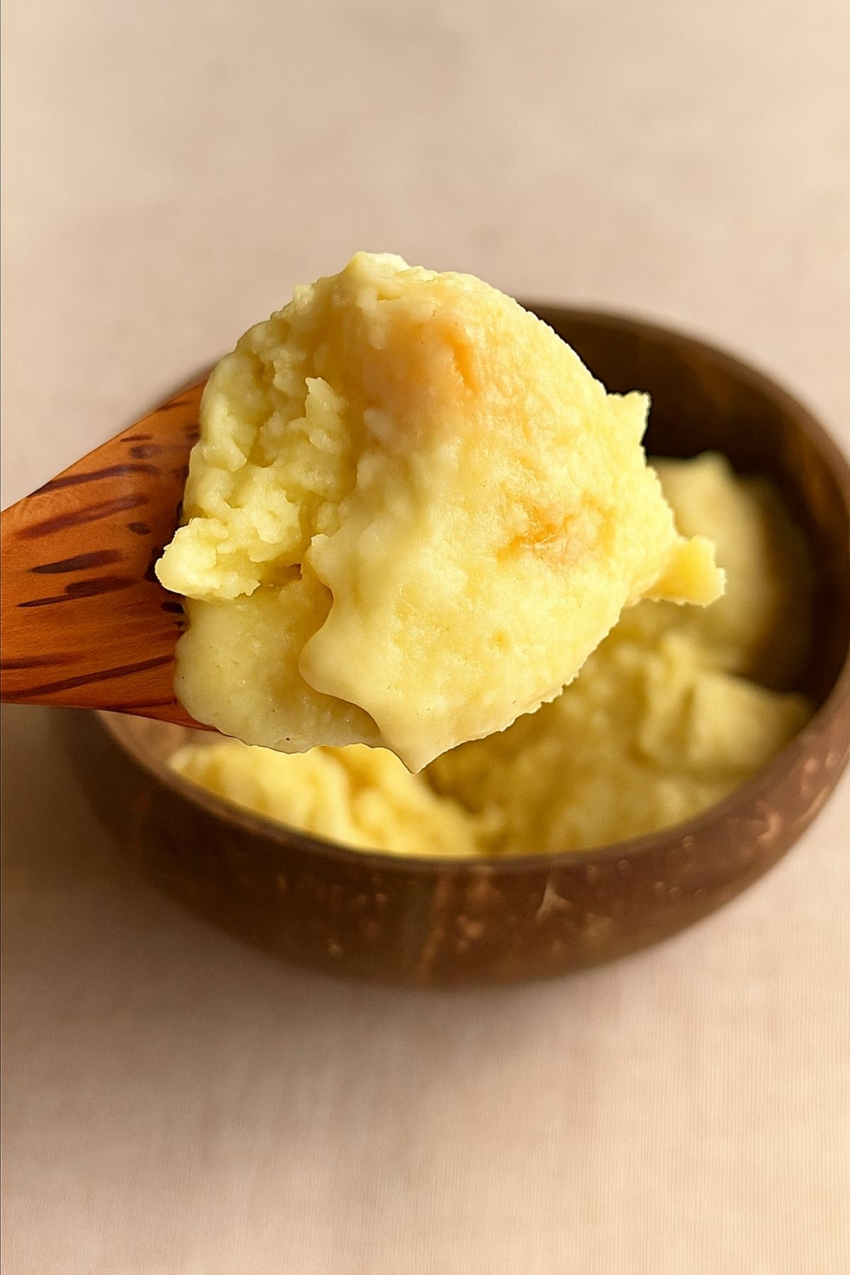 Spoonful of yellow ice cream held above a coconut bowl.