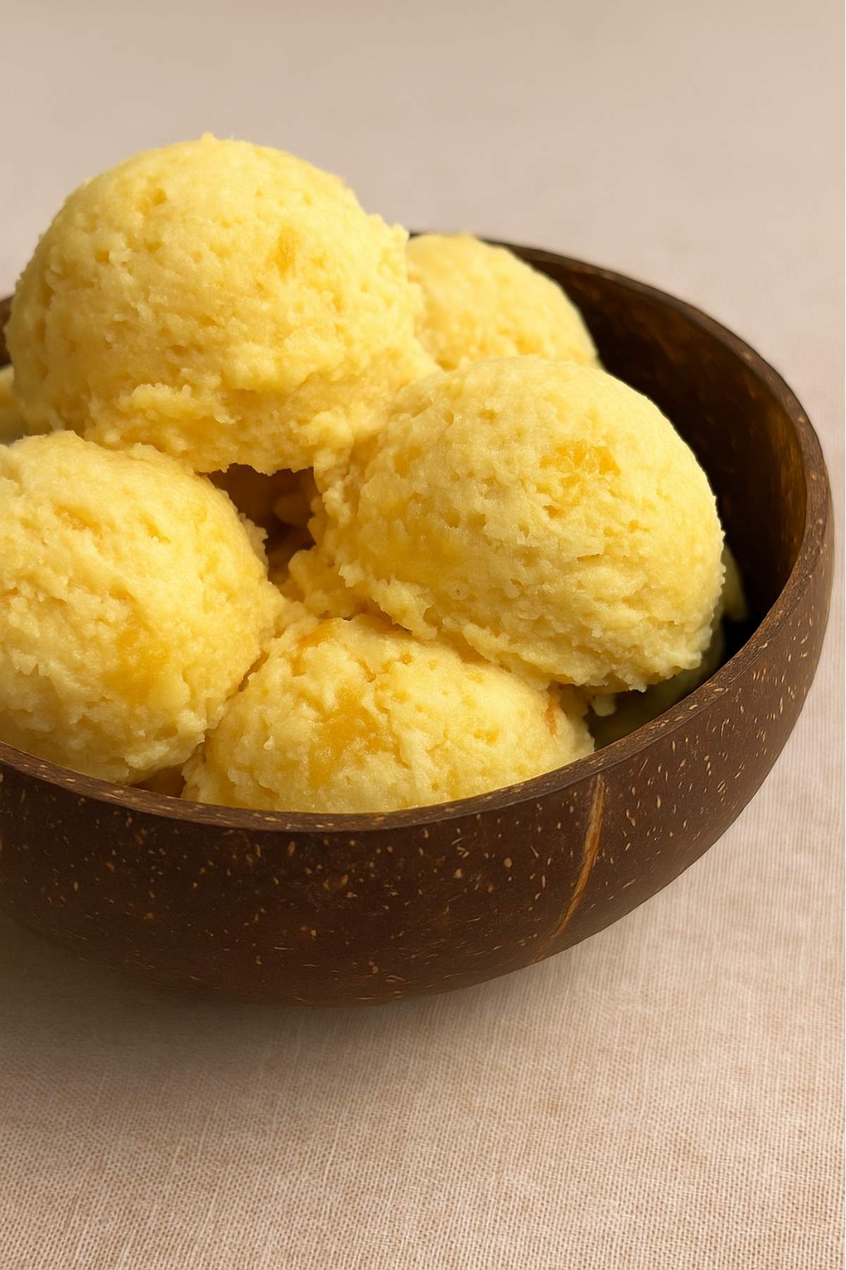 Rounded scoops of pale yellow ice cream fill a coconut shell bowl.