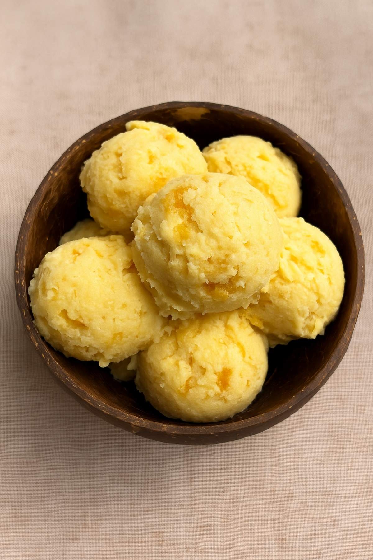 Scoops of pale yellow ice cream piled in a coconut bowl on a neutral cloth.