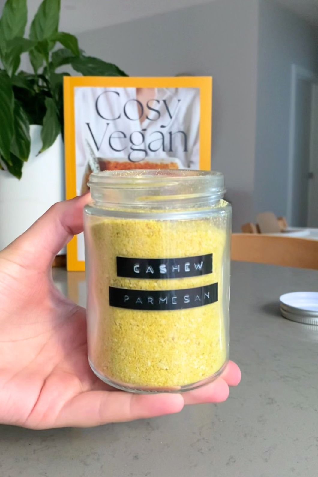 Hand holding a jar of yellow powder labeled “Cashew Parmesan.”