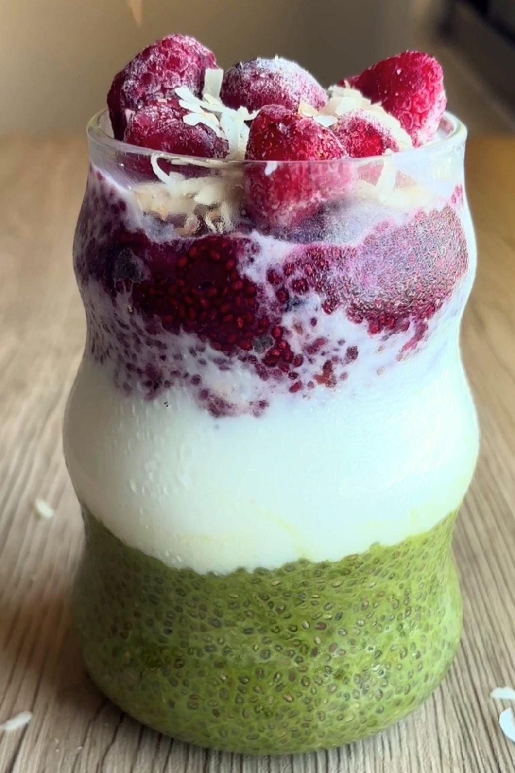 Green, white and red layers in a jar topped with raspberries and coconut flakes.