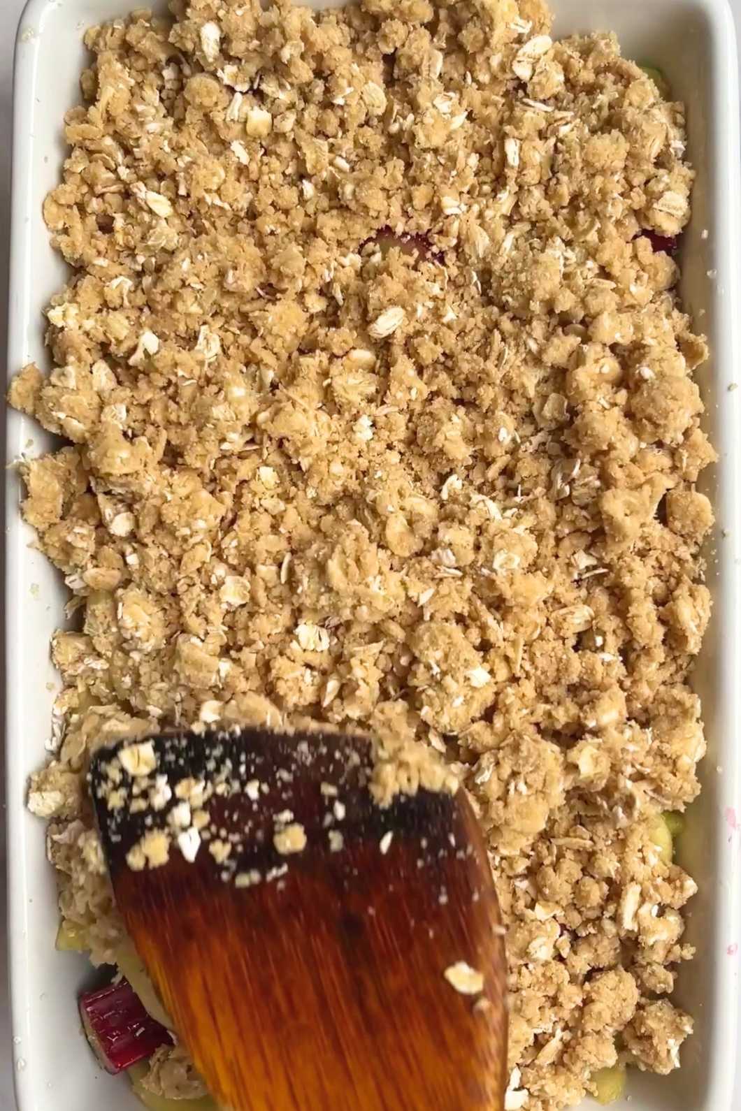 Oat crumble topping in a baking dish pressed down with a wooden spatula.