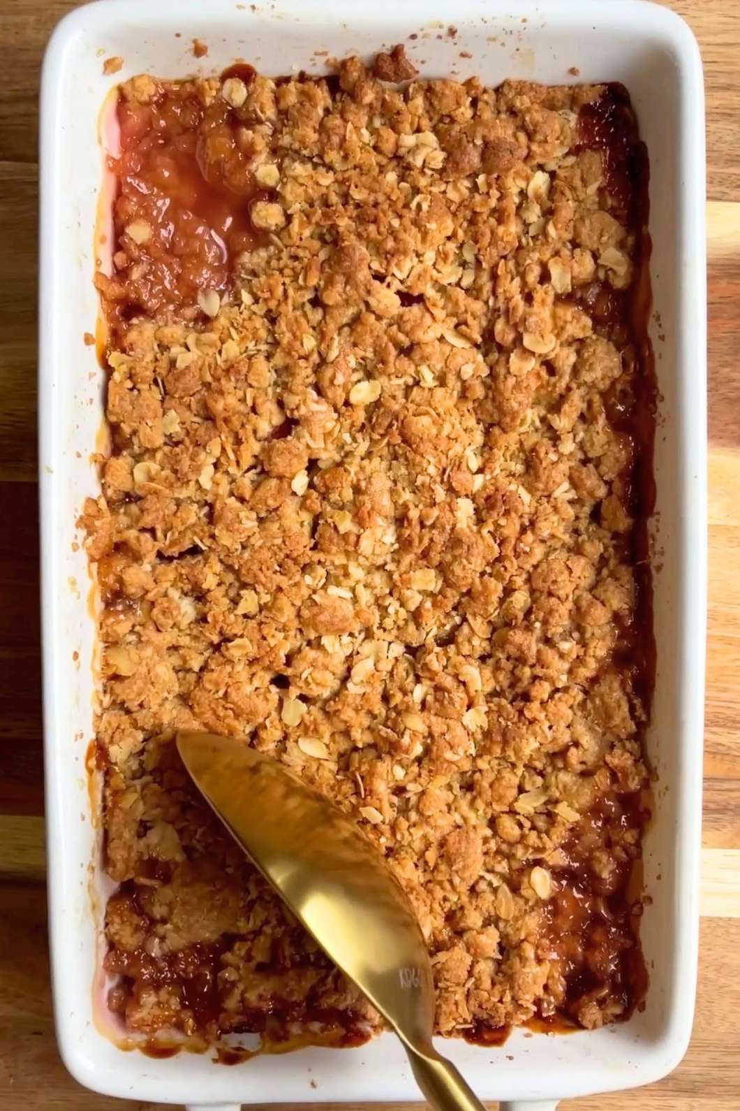 Golden crumble topping with fruit filling bubbling around the edge in a dish.