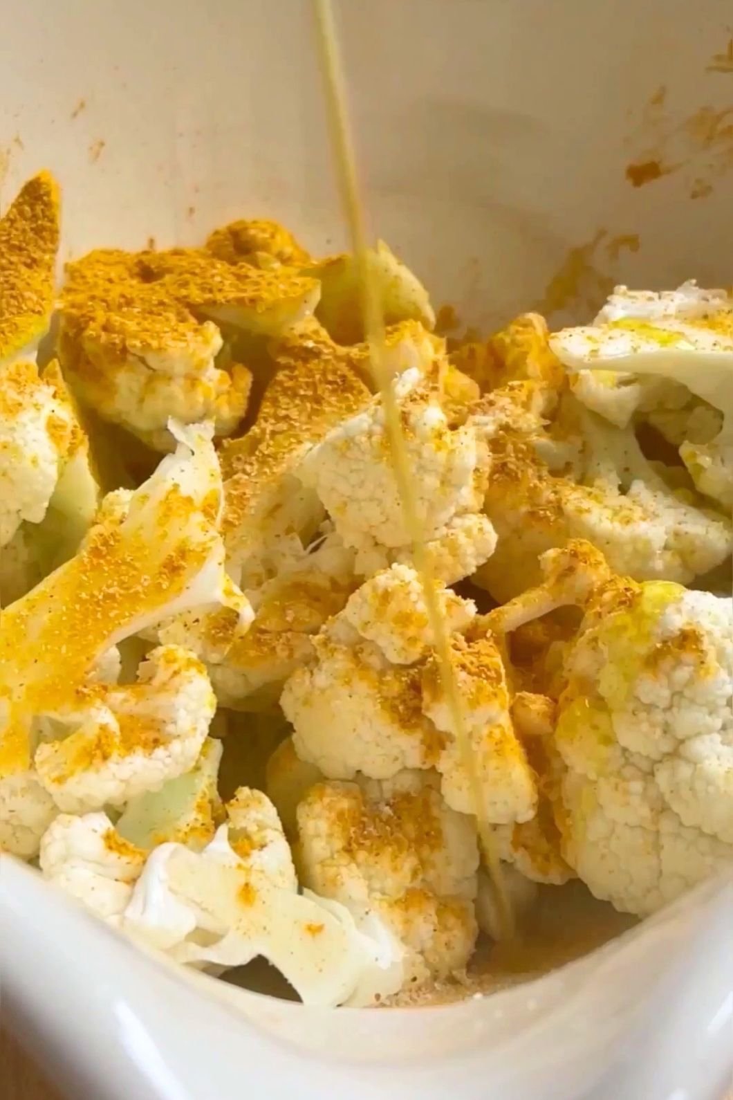 Cauliflower florets coated in golden curry spices being drizzled with oil.