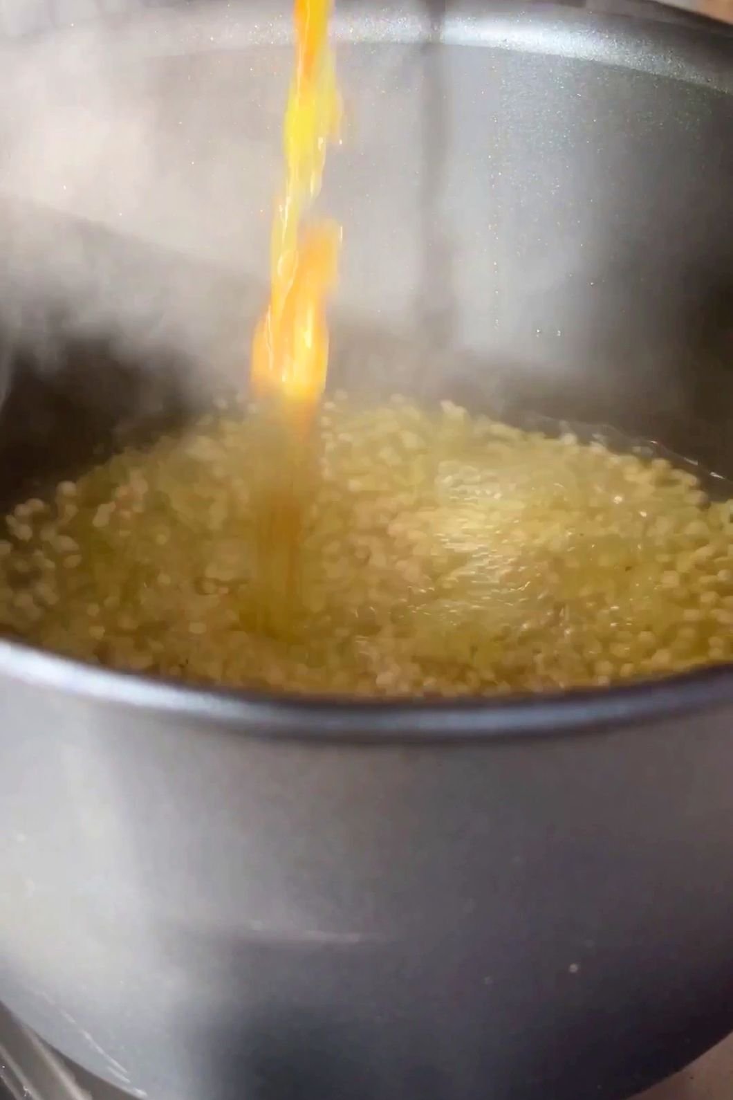 Golden broth pouring into simmering pearl couscous in a pot.
