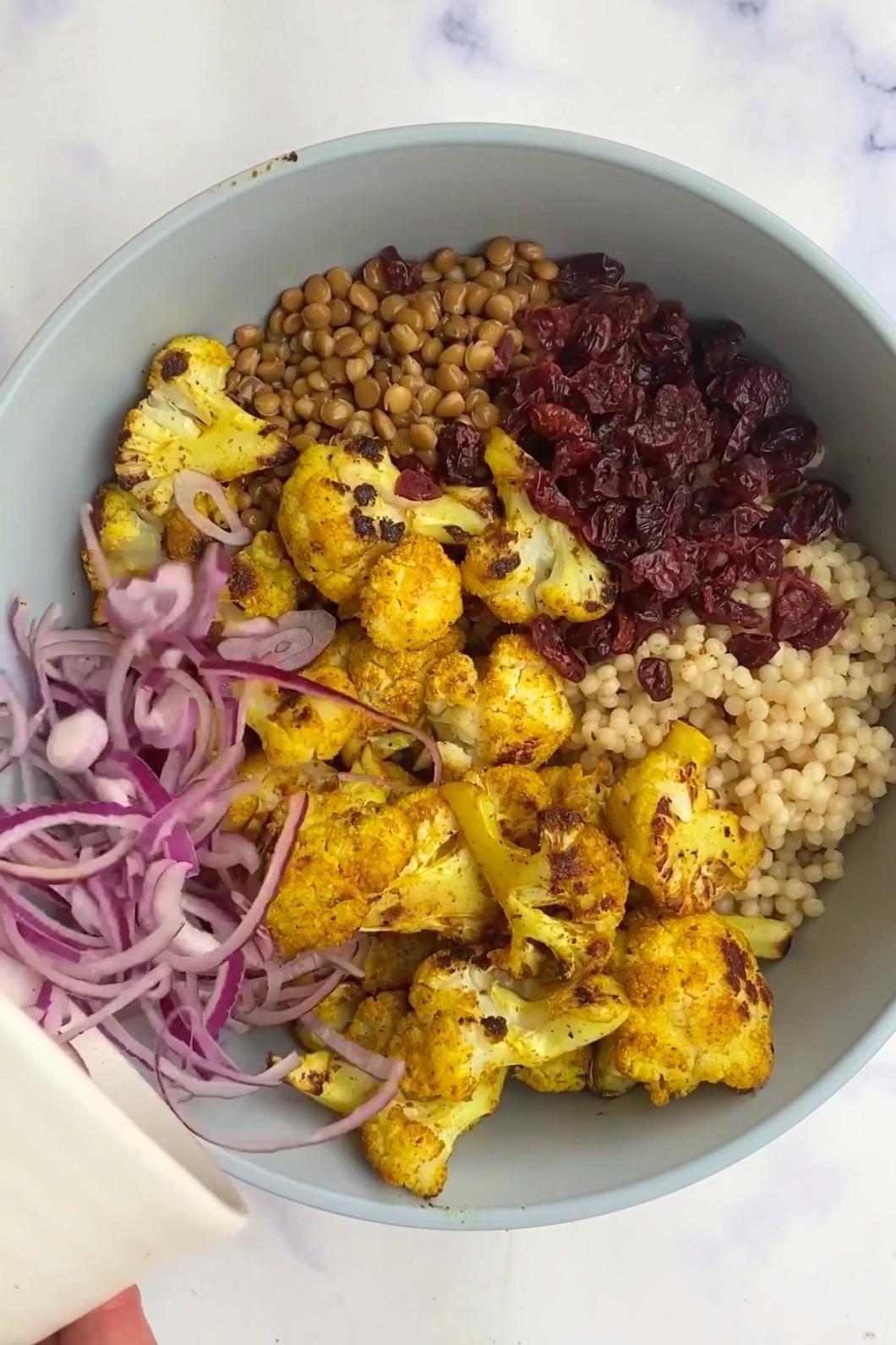 Spiced cauliflower, pearl couscous, lentils, cranberries and red onion in a bowl.