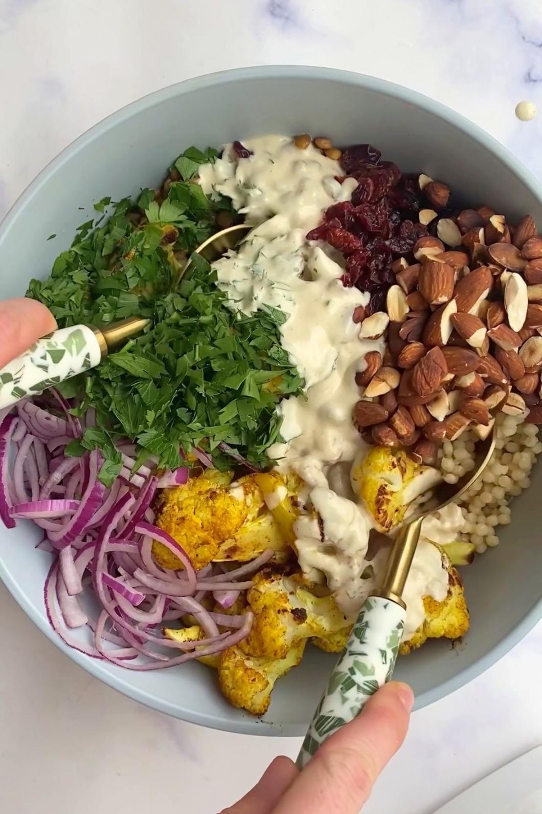 Bowl of curried cauliflower salad with pearl couscous, lentils, red onion slices, chopped parsley, almonds, cranberries and creamy dressing.