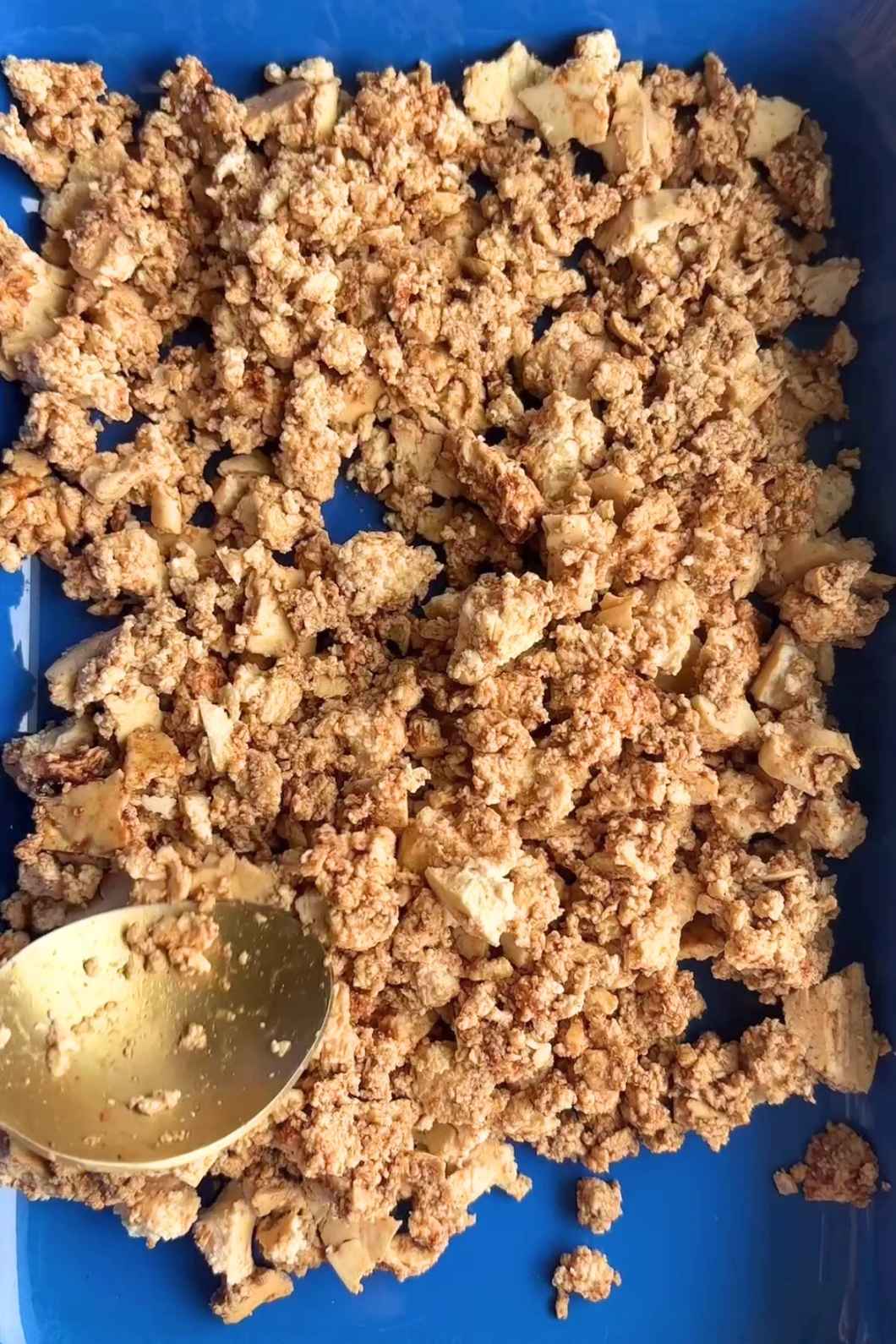 Crumbled golden-brown tofu pieces in a blue container with a spoon.