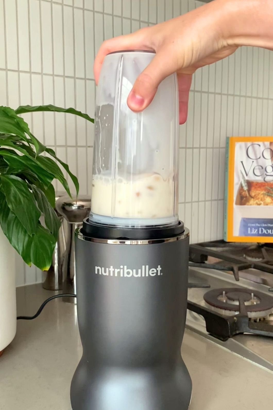 Hand holding a blender cup filled with pale liquid and bits on a NutriBullet base.