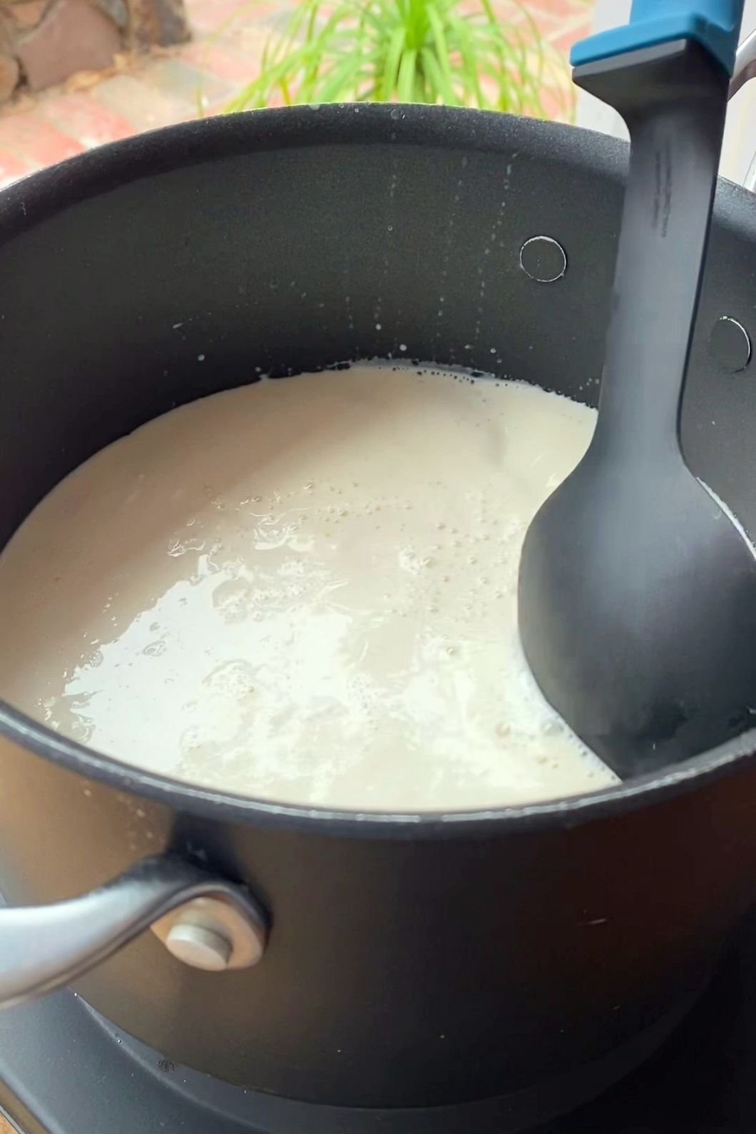 Black saucepan filled with creamy liquid being stirred by a black spatula.