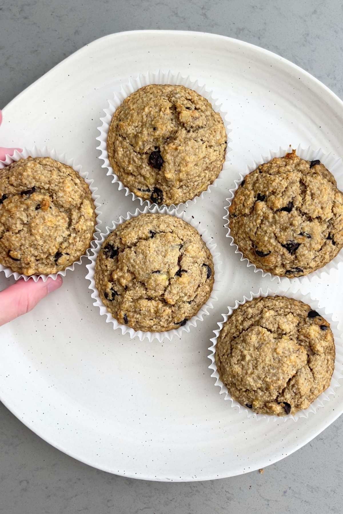 Five golden-brown muffins in white paper liners arranged on a round plate.