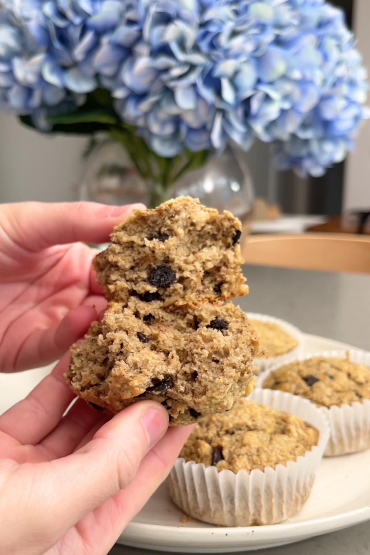 Two hands pull apart a muffin, showing its tender, chocolate-studded crumb.