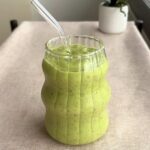 Close-up of the green smoothie in the ridged glass, highlighting tiny seed specks in the drink.